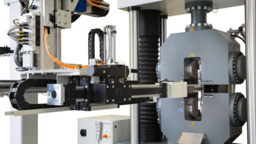 Sistema de ensayos automatizado roboTest P durante la alimentación de una probeta de metal en una máquina de ensayos de materiales